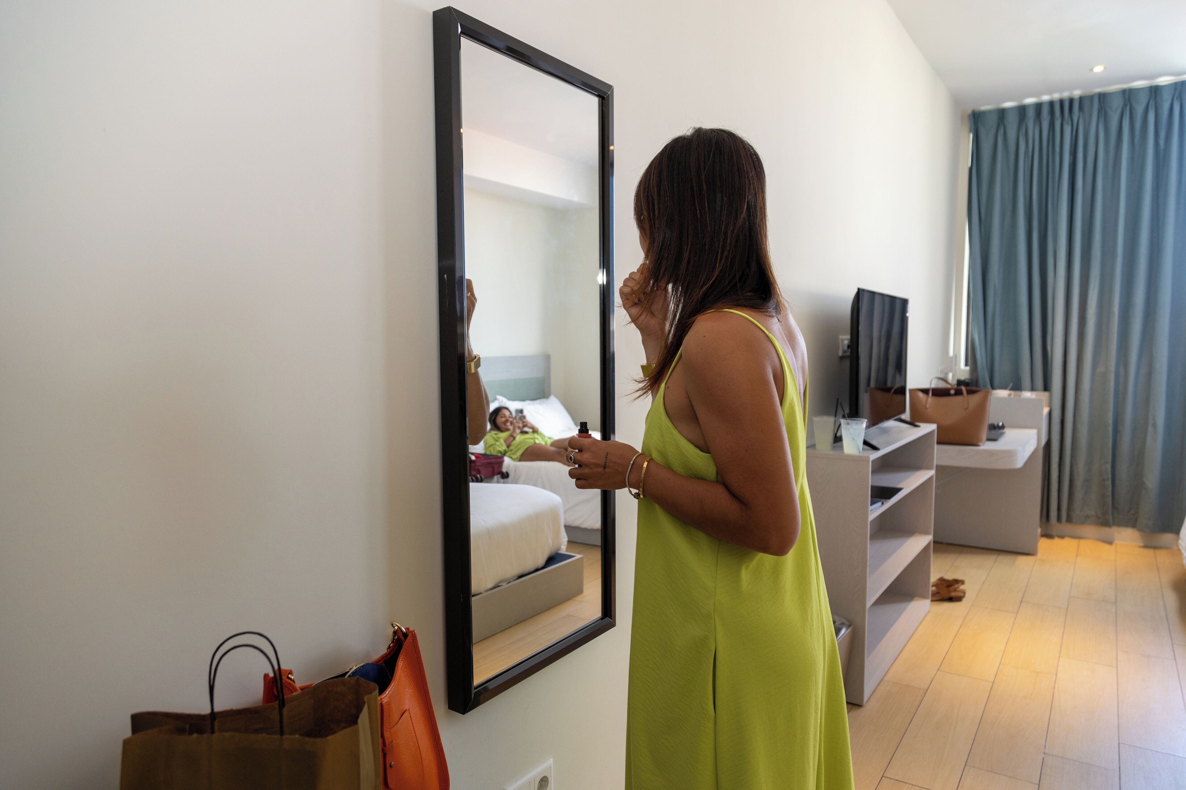 A hotel room with a large mirror, a bed, a TV, and a desk.