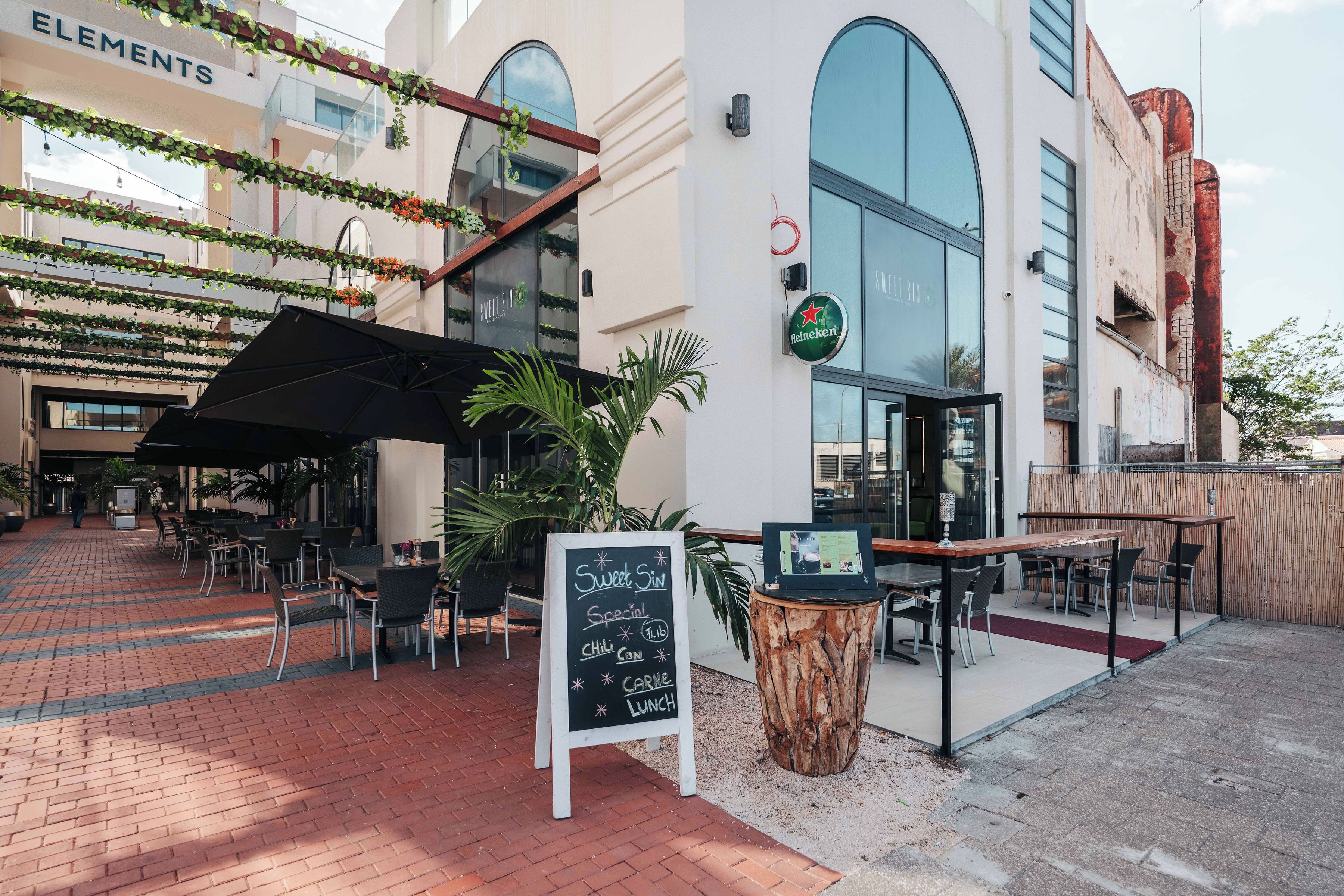 An outdoor seating area with tables and chairs, a chalkboard menu, and a Heineken sign.