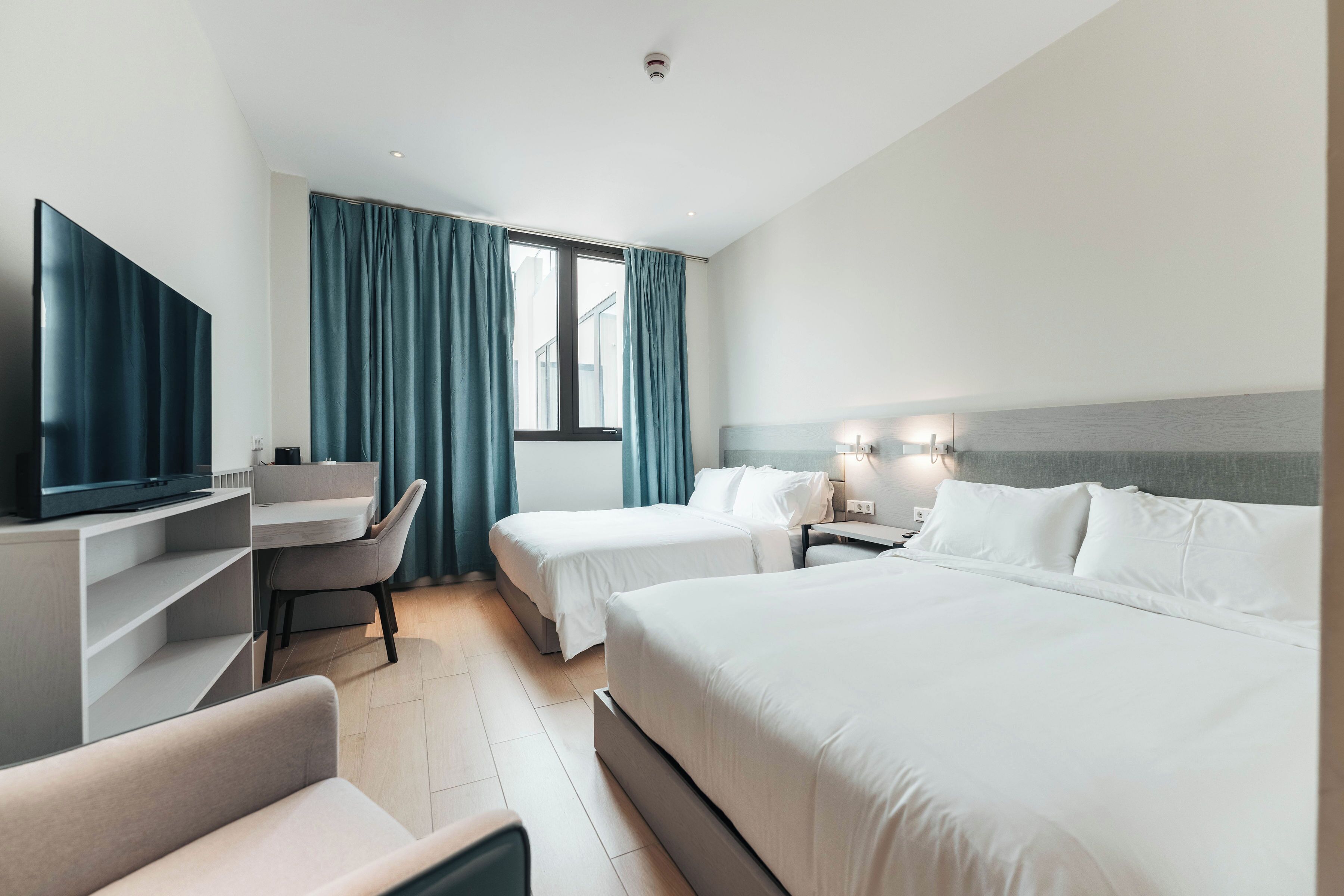 Een hotelkamer met twee bedden, een bureau, een televisie en een raam met gordijnen.