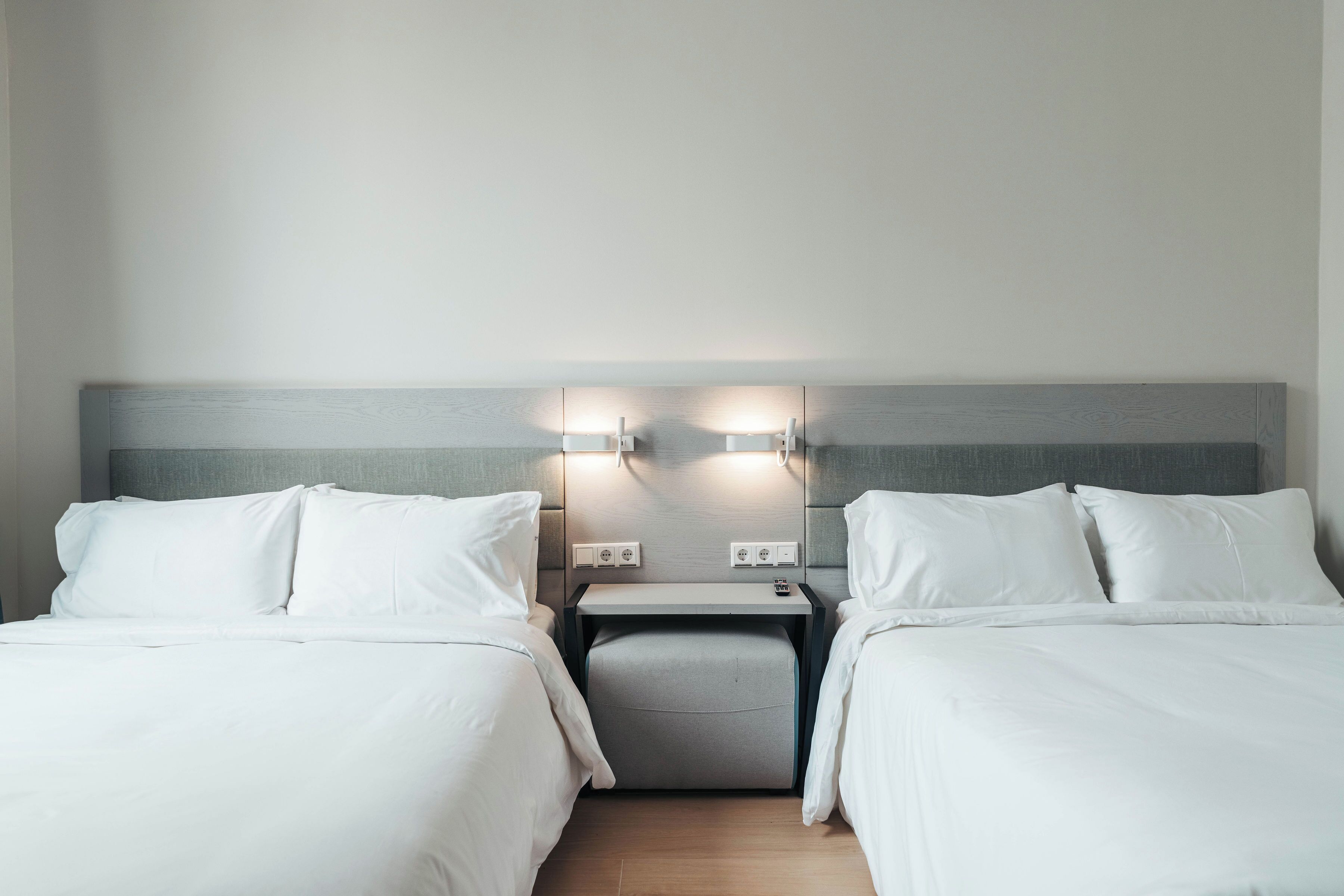 A hotel room with two single beds, a small bedside table, and a nightstand with two wall-mounted lamps.