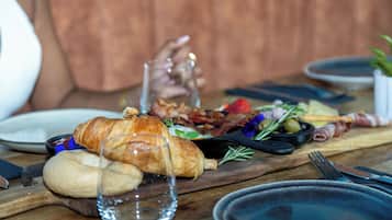 A wooden table with a variety of food items including bread, a croissant, and some vegetables.