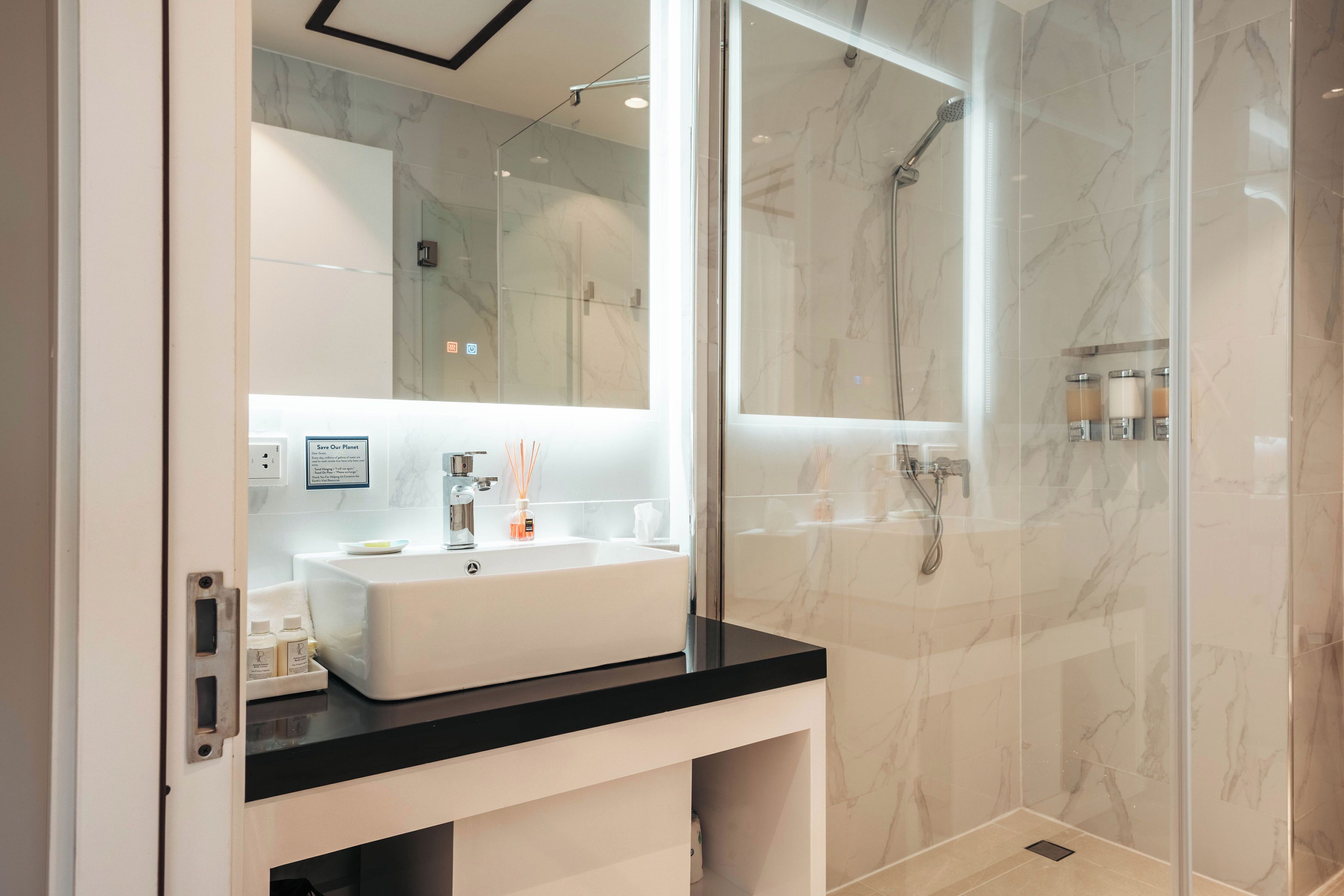 Une salle de bain moderne avec un lavabo blanc, un plan de toilette noir et une douche séparée par des parois en verre.