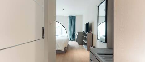 Una habitación de hotel moderna con cama, escritorio, cómoda y un espejo grande.
