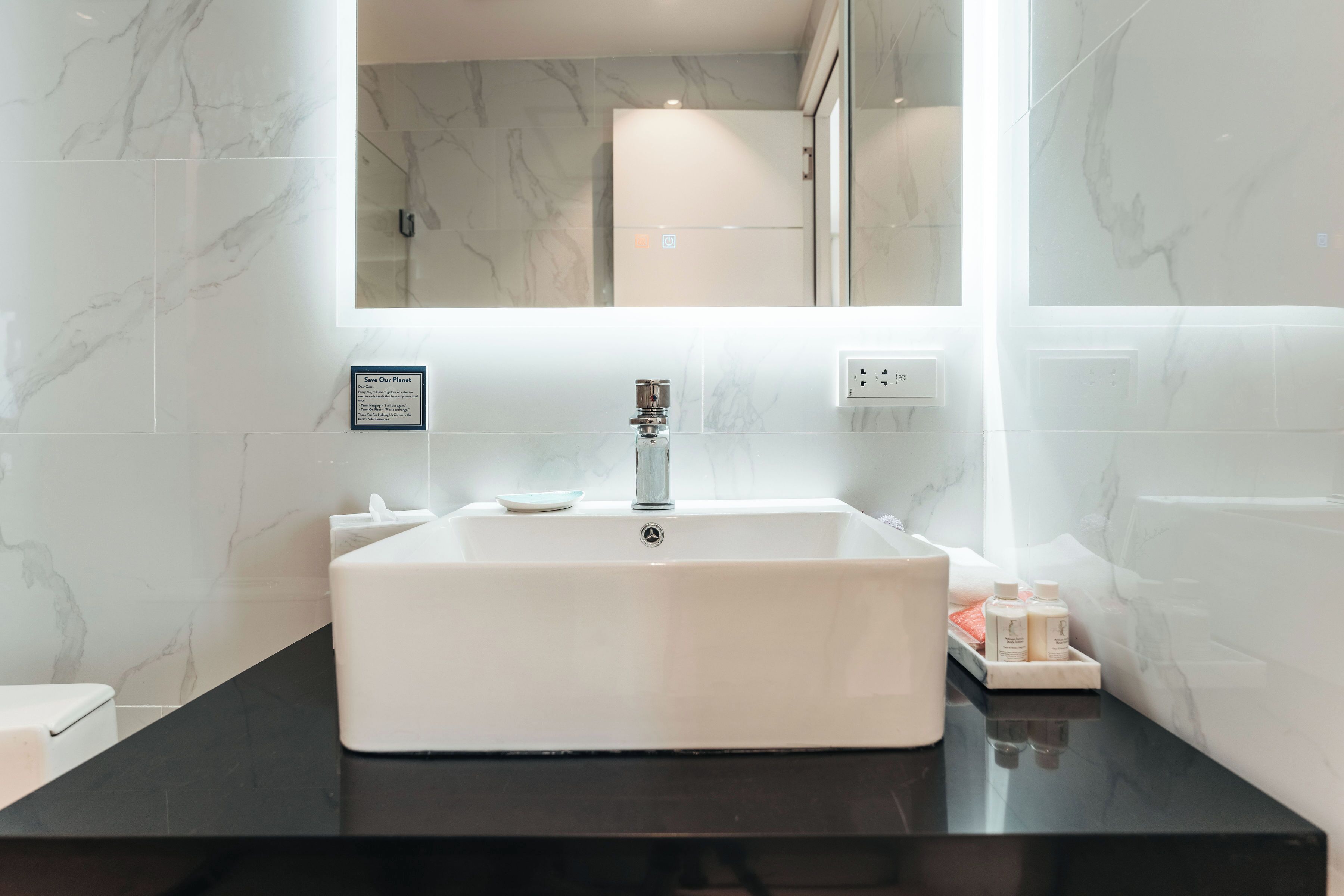Une salle de bain avec un lavabo blanc, un plan de toilette noir et des murs en marbre.