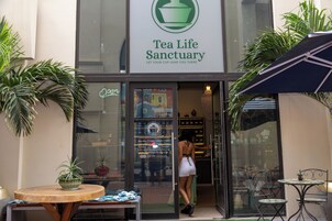 Exterior del Santuario Tea Life, con puerta de vidrio, un letrero y plantas en macetas.