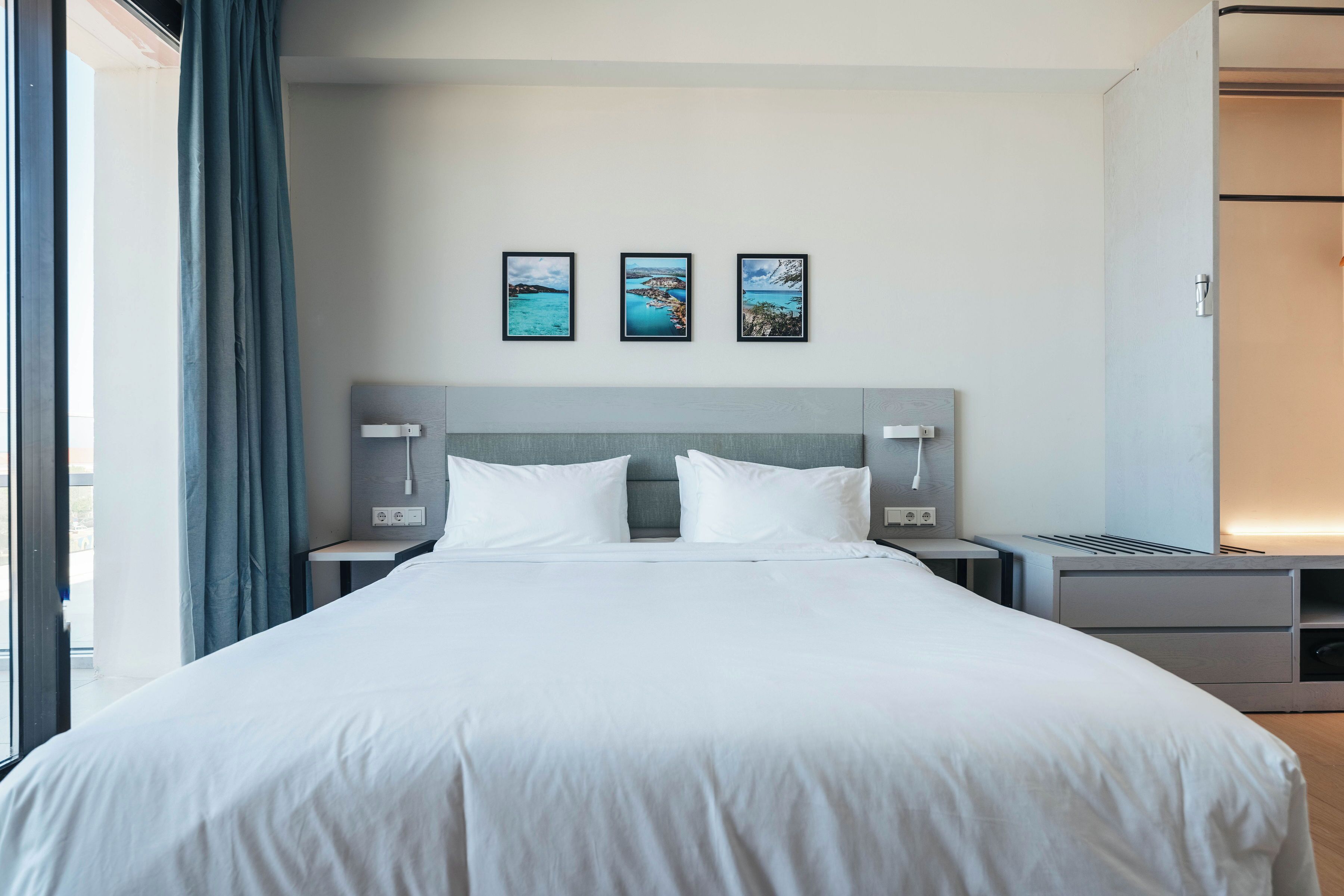 A modern hotel room with a large bed, a headboard, bedside tables, and a view of the sea through the window.