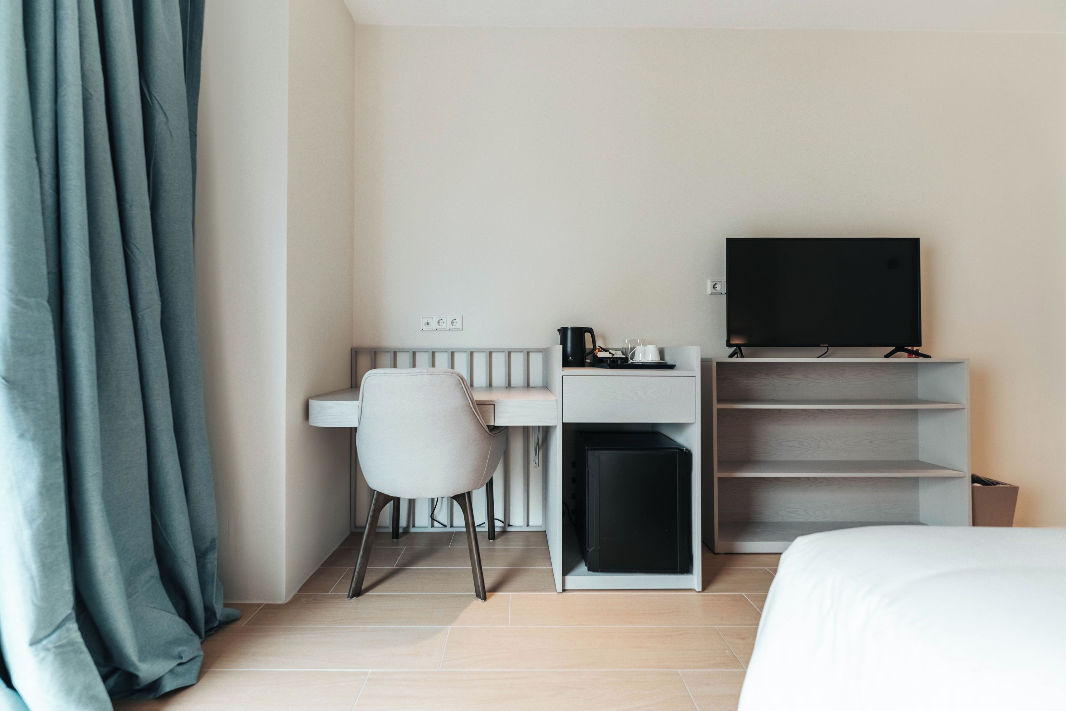 A hotel room with a bed, a desk with a chair, a television, and a small cabinet.