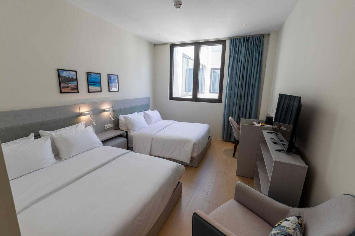 A hotel room with two beds, a desk, a chair, and a large window with curtains.