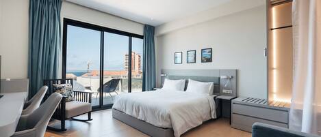 Ein modernes Hotelzimmer mit einem großen Bett, einem Schreibtisch, einem Sessel und Blick auf die Stadt.