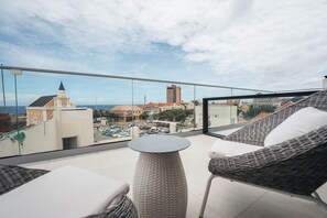 A balcony with wicker furniture, a round table, and a view of buildings and parked cars. - Elements Hotel & Shops (Willemstad)