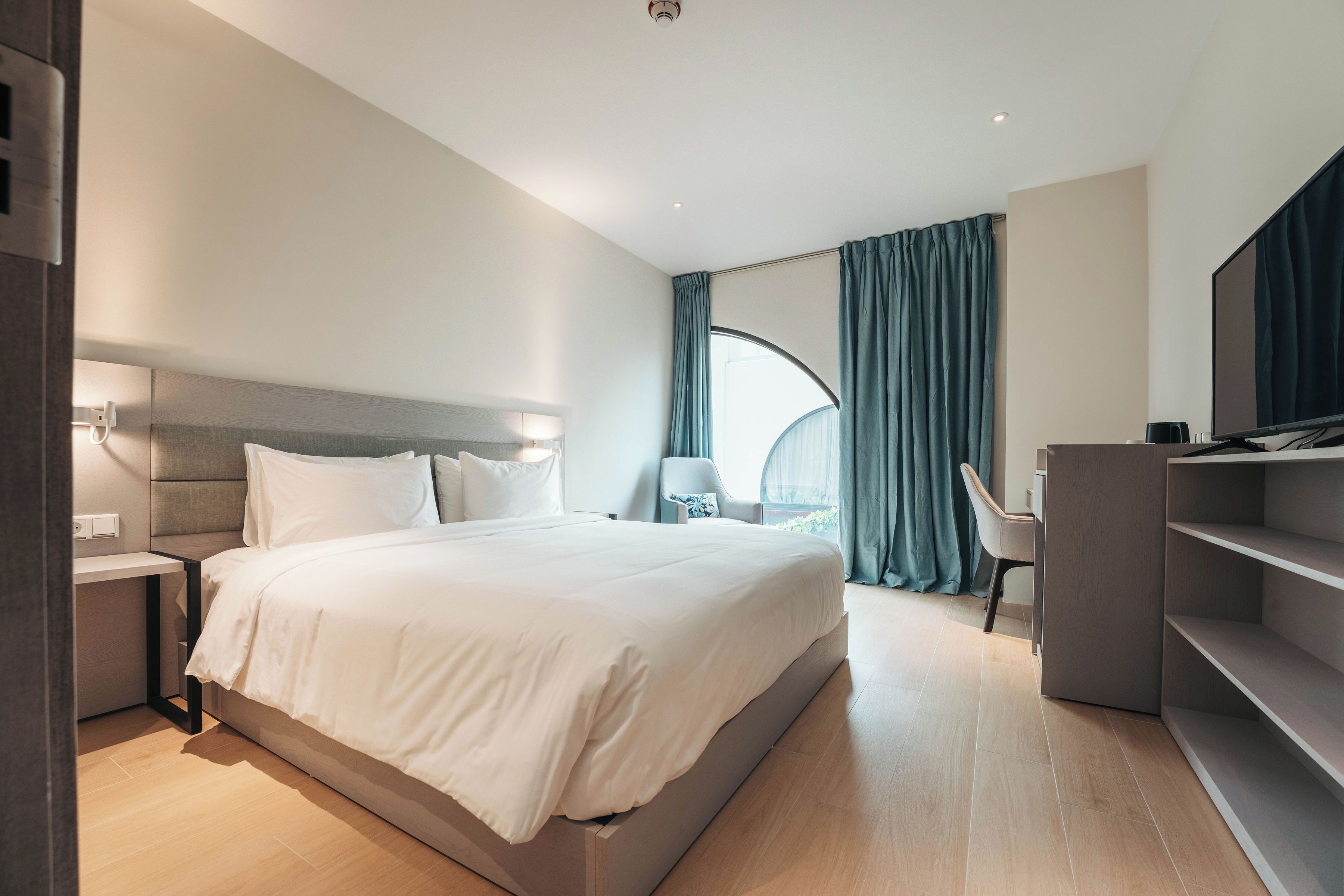 A modern hotel room with a large bed, a desk, a chair, and a TV.