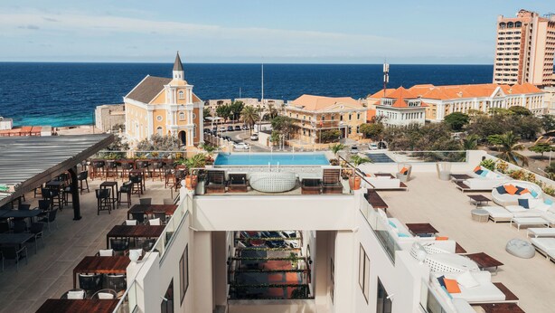 Un área de piscina en la azotea con sillas de descanso y vista al océano.