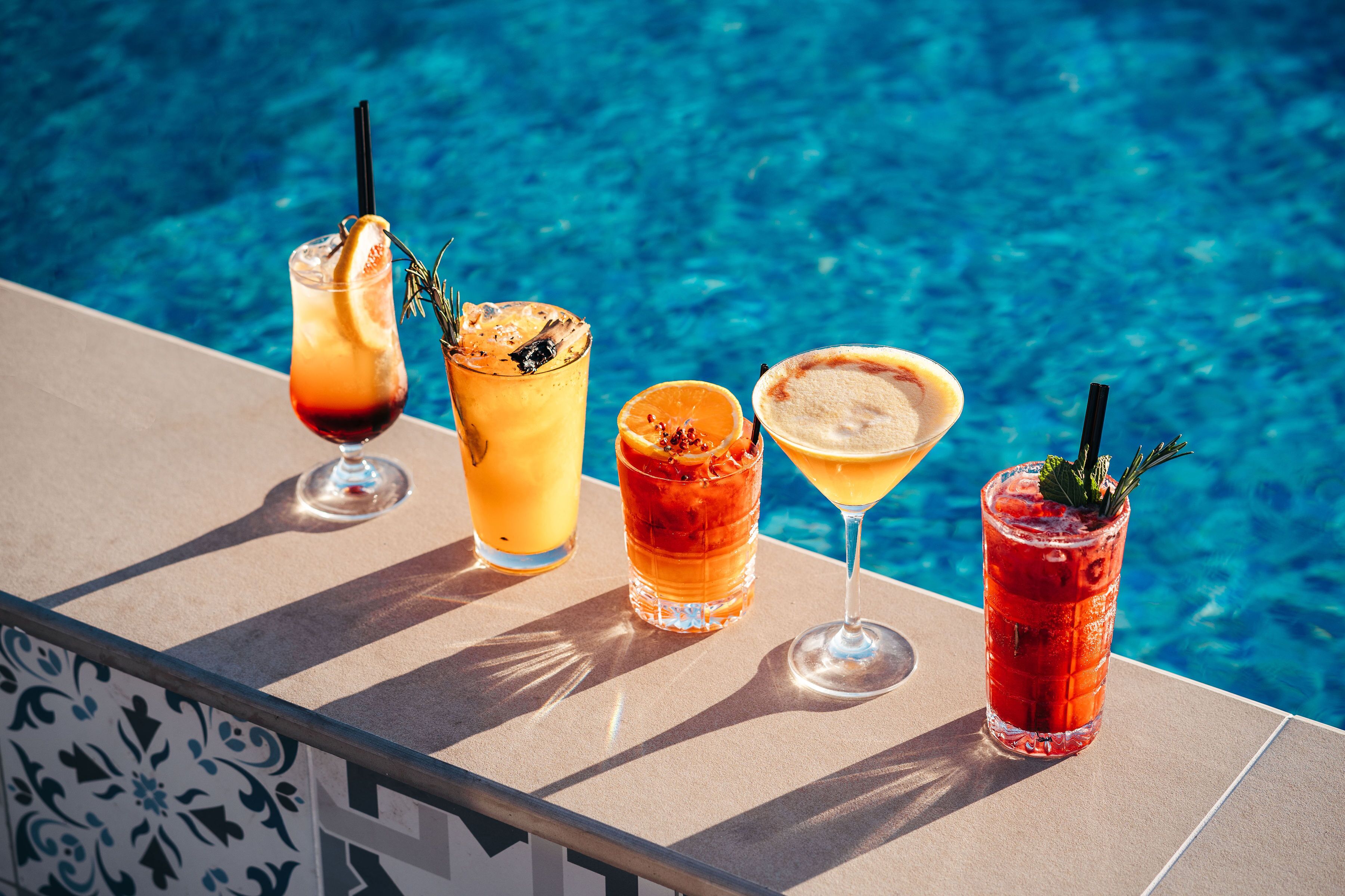 Quatre cocktails sont posés sur une table, près d’une piscine.