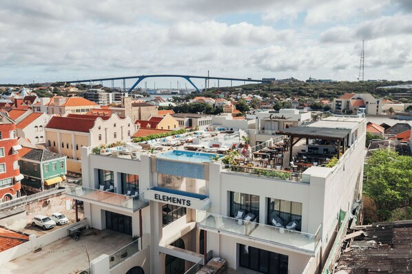 A rooftop bar with a pool, a sign reading "ELEMENTS", and a view of the cityscape including a bridge. - Elements Hotel & Shops (Willemstad)