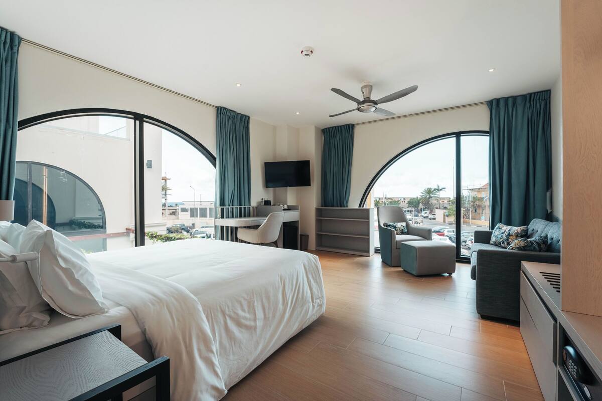 A modern hotel room with a large bed, a desk, a sofa, and a TV.