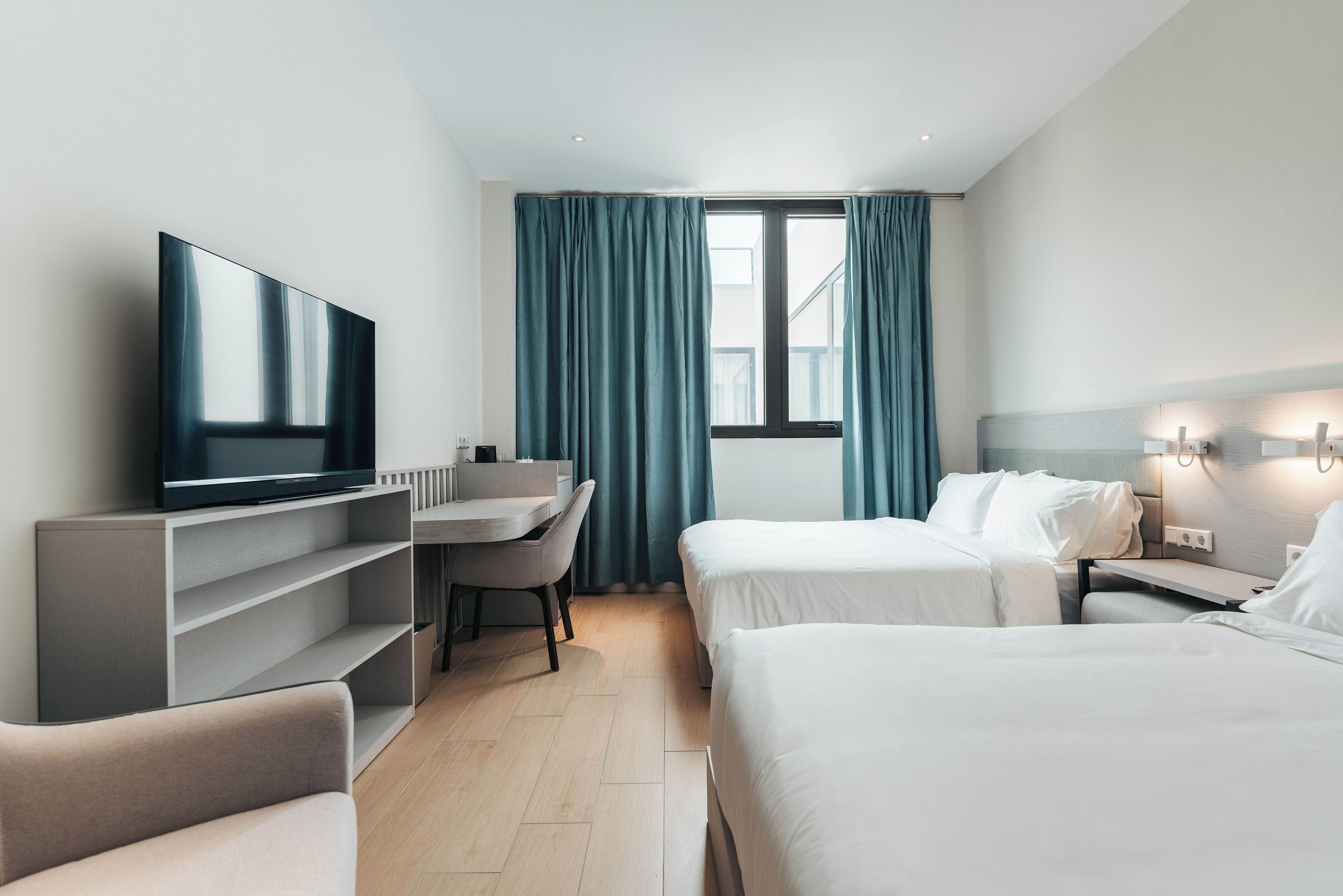 A hotel room with a bed, a desk, a chair, a TV, and a window with curtains.