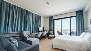Habitación de hotel moderna con una cama grande, un escritorio y un sofá. Se ve la ciudad a través de amplias ventanas.