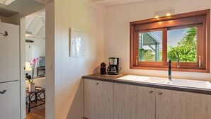 A modern kitchen with a built-in sink, a coffee maker, and a window with a view of greenery. - Marigot Bay Luxury villa (St Barths)