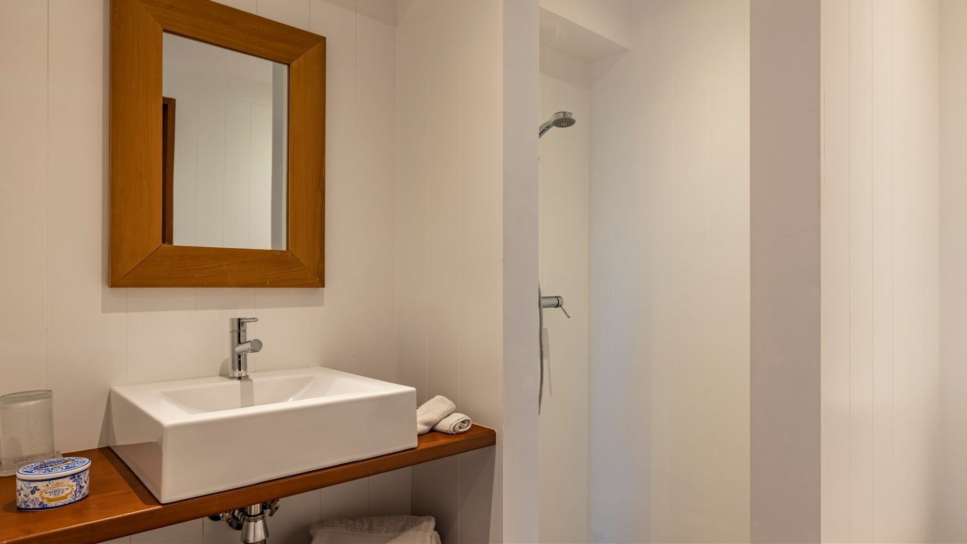 A bathroom with a white sink, a wooden vanity, a mirror, and a shower area.