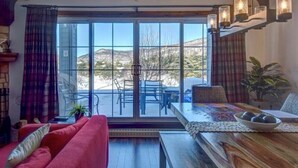 Ein modernes Wohnzimmer mit einem roten Sofa, einem Holzespeisetisch mit einer Fruchtschale und Blick auf Berge durch große Glastüren.