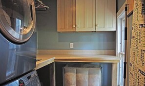 A compact kitchen with wooden cabinets, a built-in washing machine, and a small window. - The Shire- 5 minutes from Cooperstown, the Dreams Park and induction! (Milford)