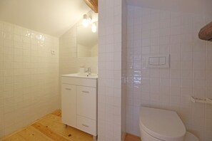 Een badkamer met witte tegels, een houten vloer, een wastafel met spiegel en een toilet.