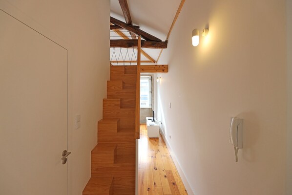 A narrow hallway with wooden flooring and a staircase leading to a room with a window.