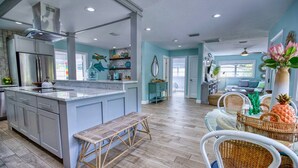 Una cocina amplia con una isla grande, suelo de madera y un comedor con mobiliario de mimbre.