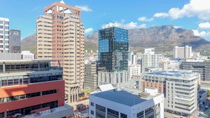 Un paysage urbain avec des bâtiments modernes, dont un imposant bâtiment rouge doté de balcons et un gratte-ciel en verre.