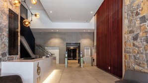Un espace d’accueil avec un mur en pierre, un comptoir de réception, un escalier et un coin salon.