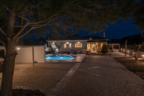 Una casa con piscina, zona de estar exterior e iluminado patio.