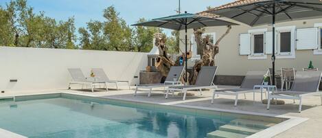 A swimming pool with lounge chairs and a large umbrella.