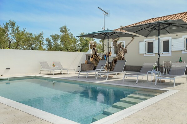 Una piscina con sillas de descanso y un parasol grande.