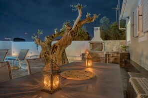 An outdoor dining area with a tree centerpiece, two lanterns, and a pool in the background.