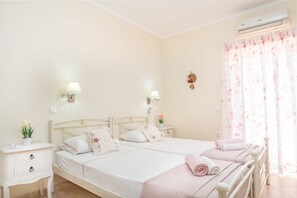 Habitación de hotel con dos camas, una mesita de noche, una lámpara de pared y una ventana con cortinas florales.