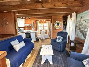 A cozy cabin interior with a blue sofa, a small dining table, a chair, and a kitchen area.