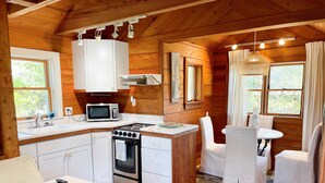 A compact kitchen with a microwave, stove, and sink. There is a dining area with a table and chairs. - The Back House:  Quaint two bedroom Ocracoke Island cottage (Ocracoke)