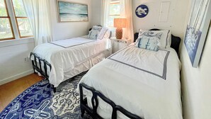 A bedroom with two beds, a large window, a painting, and a decorative plate on the wall. - The Back House:  Quaint two bedroom Ocracoke Island cottage (Ocracoke)