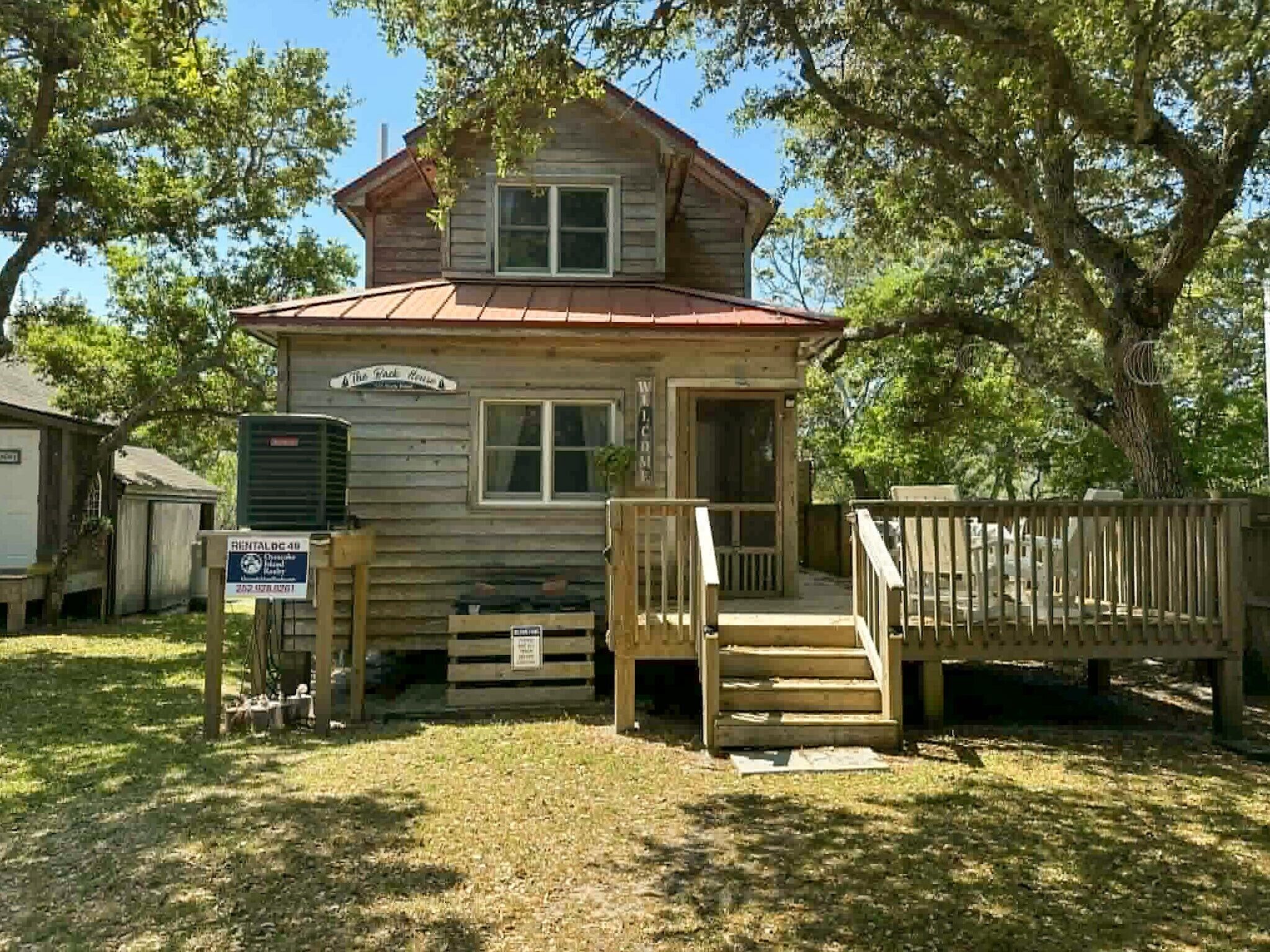 A wooden cabin with a porch, a sign indicating rental availability, and a mailbox.