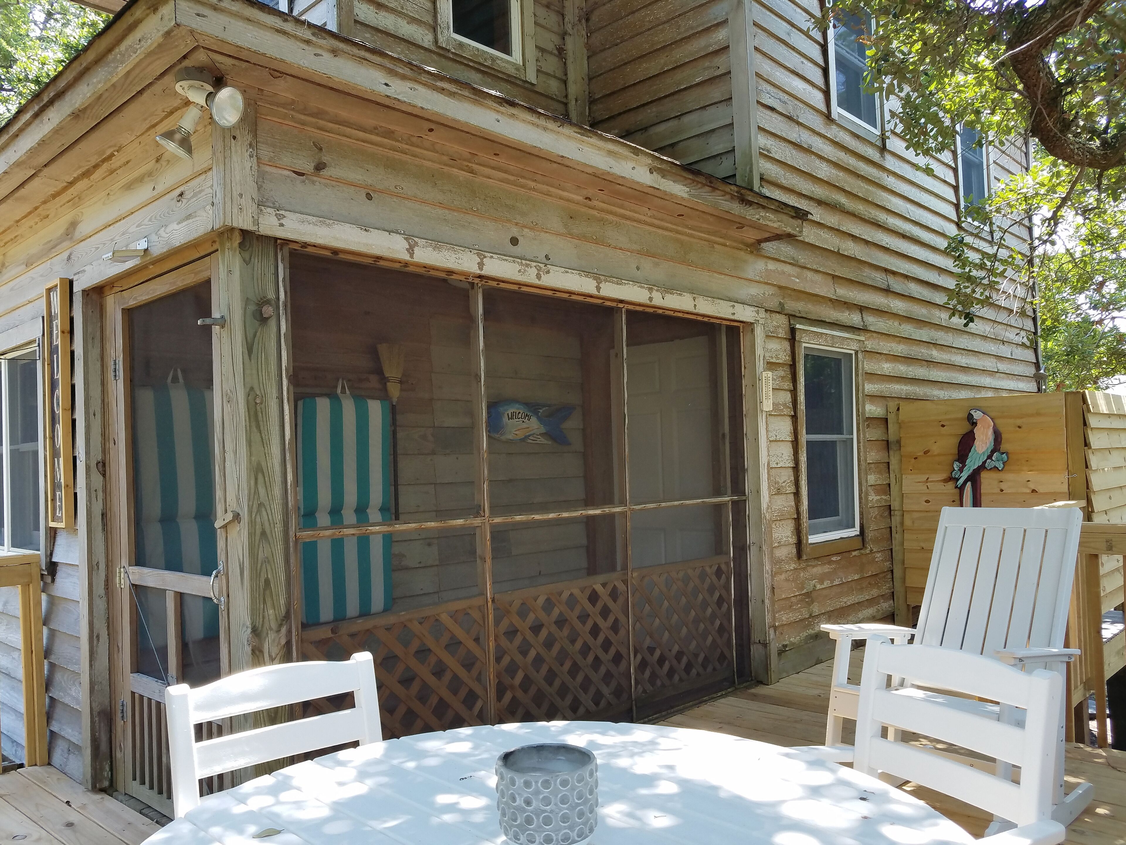 A rustic wooden cabin with a screened porch, two white chairs, and a table.