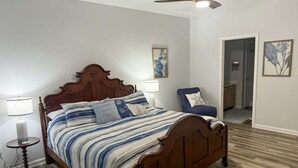 A bedroom with a wooden bed, two bedside lamps, a ceiling fan, and a chair with a pillow.