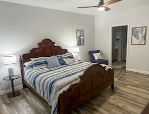 Une chambre à coucher avec un lit en bois, deux lampes de chevet, un ventilateur de plafond et une chaise avec un coussin.
