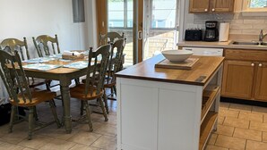 A kitchen with a dining area, wooden cabinets, a white island, and a ceiling fan. - Hydeaway: Convenient to Restaurants, Shops and Silver Lake (Ocracoke)