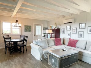 A living room with a white sofa, a wooden coffee table, and a dining area with a table and chairs. - Marsh Mellow: Expansive Marsh Views (Ocracoke)