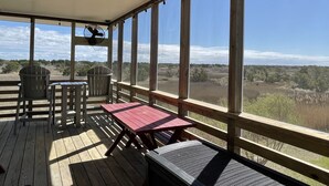 Une terrasse extérieure couverte, dotée d’une table et de chaises, de grandes fenêtres et offrant une vue sur le paysage.