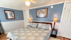 Une chambre à coucher avec un lit, deux lampes de chevet, un ventilateur de plafond et un tableau accroché au mur.