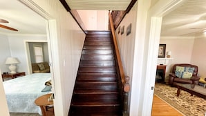Un escalier en bois mène à une chambre à coucher qui contient un lit, une table de chevet et une lampe.