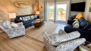 A living room with a wooden ceiling, a ceiling fan, a sofa set, a coffee table, and a television. - Sass-Sea Views: Amazing views, decks, screened porch, rooftop deck (Ocracoke)