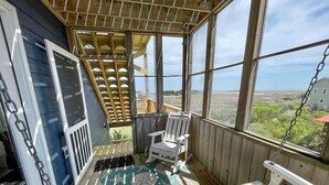 A covered porch with a wooden chair, a patterned rug, and a view of the landscape. - Sass-Sea Views: Amazing views, decks, screened porch, rooftop deck (Ocracoke)
