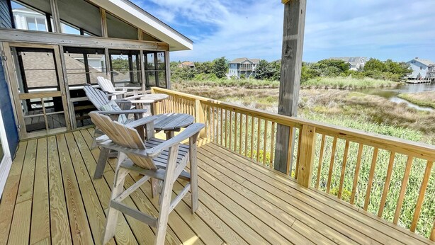 A wooden deck with outdoor seating and a view of a marshy area. - Sass-Sea Views: Amazing views, decks, screened porch, rooftop deck (Ocracoke)